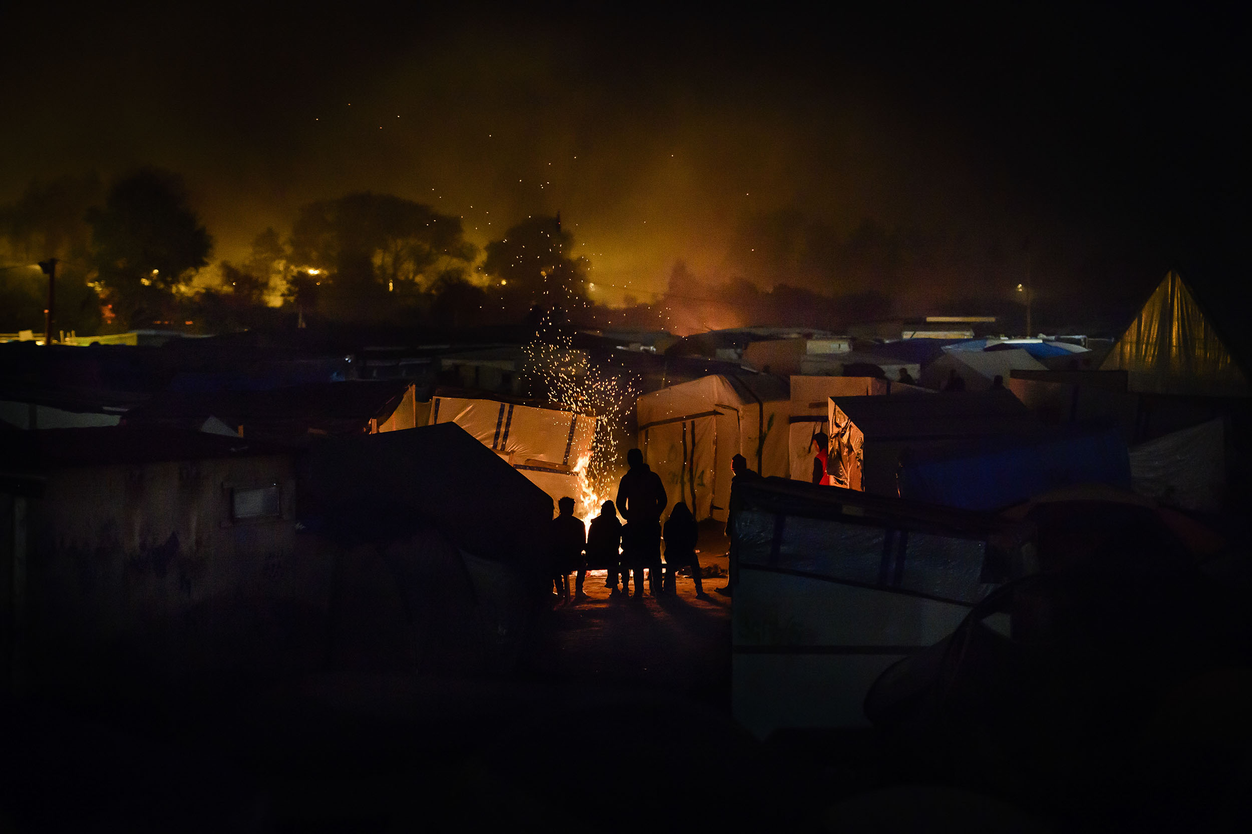 24/10/2016. Calais, France. A group of young migrants sit around a camp fire on the eve of the demolition of the migrant camp in Calais, known as the 'Jungle'.