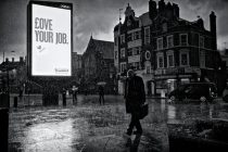 A heavy downpour of rain soaks pedestrians as they pass an illuminated advertising sign saying "Love Your Job". Hammersmith, London. January 14, 2011. Photo: Edmond Terakopian