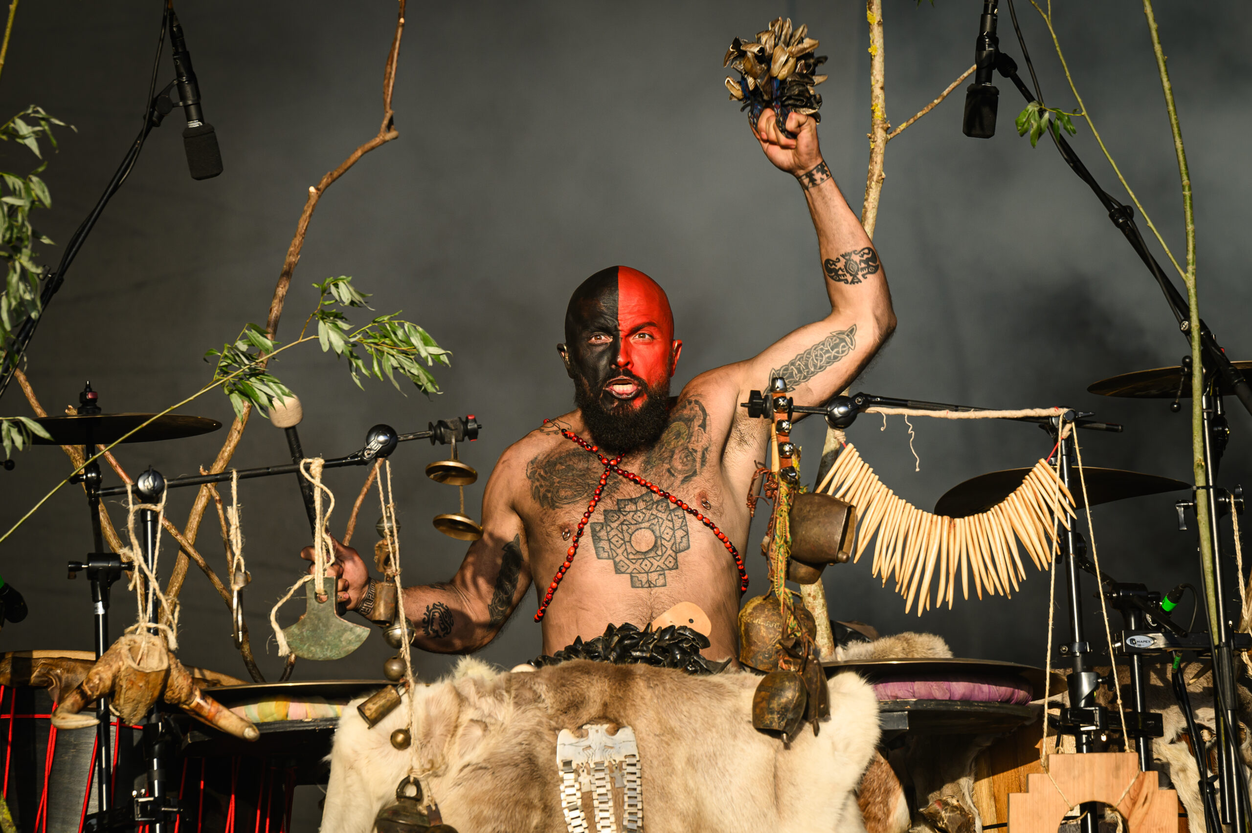 A member of the German group Heilung plays traditional tribal drums as they perform on the West Holts stage during day three of Glastonbury Festival 2024 at Worthy Farm, Pilton on June 28, 2024 in Glastonbury, England. The drummer has a painted face and is staring straight into the camera as he plays.