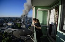 © Licensed to London News Pictures. 14/06/2017. London, UK. A woman looks out from her balcony at the scene of a huge fire at Grenfell tower block in White City, London. The blaze engulfed the 27-storey building with 200 firefighters attending the scene. There were reports of people trapped in the building. Photo credit: Ben Cawthra/LNP
