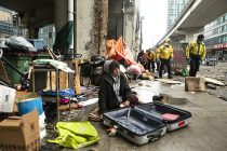 A person experiencing homelessness sits by an encampment as police officers move in to help city workers clear the encampment  on  Toronto's Bay Street, on Friday May 15, 2020. The city is clearing homeless camps in downtown Toronto as part their COVID strategy. THE CANADIAN PRESS/Chris Young